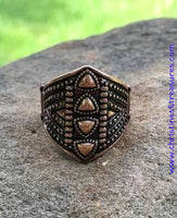 Bronze shield-shaped ring with intricate design on a stone surface