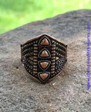 Bronze shield-shaped ring with intricate design on a stone surface