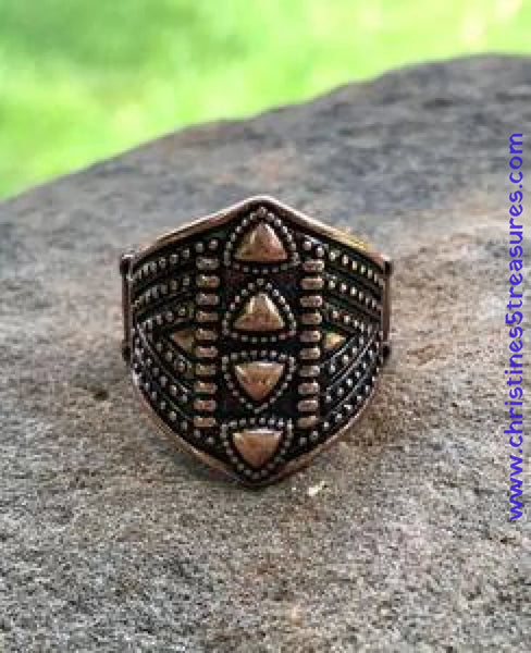 Bronze shield-shaped ring with intricate design on a stone surface